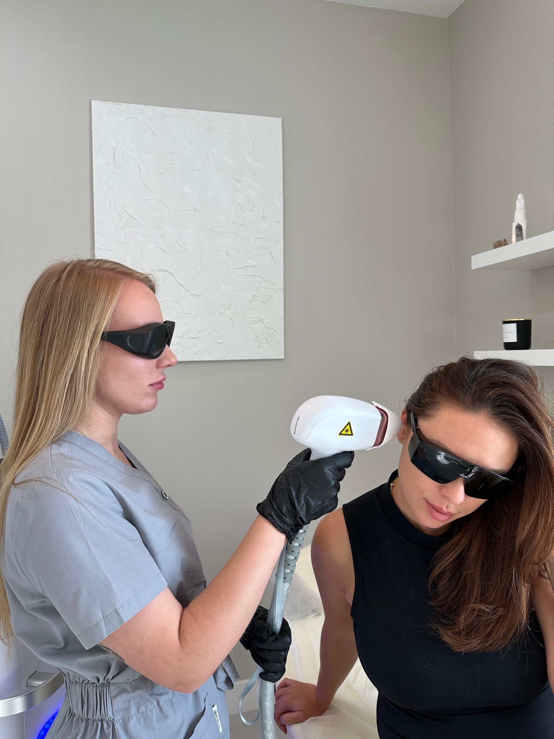 Woman receiving laser hair removal treatment on her face. Practitioner holding device. Both wear protective eyewear.