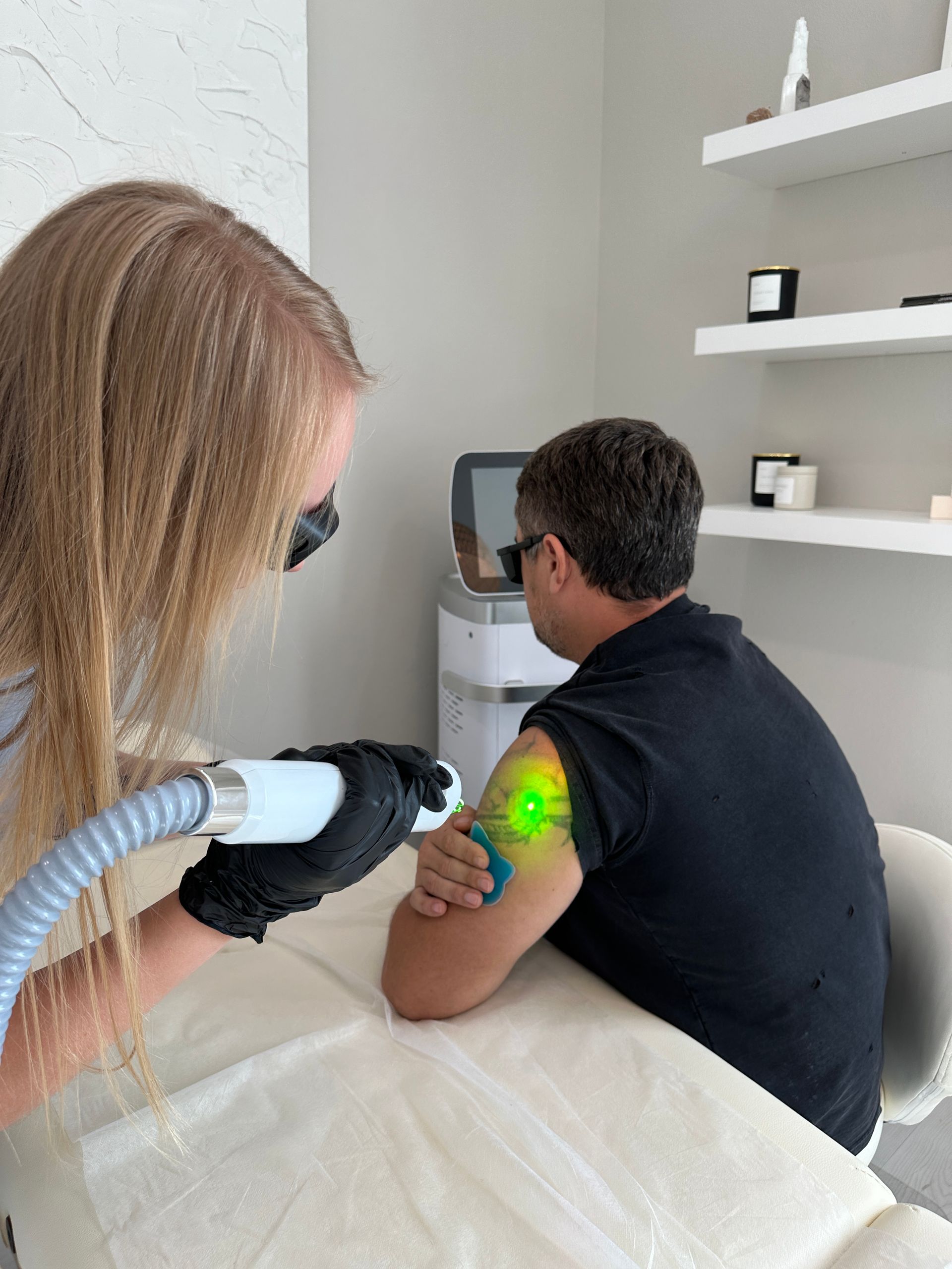 A man is getting a tattoo removed from his arm by a woman.