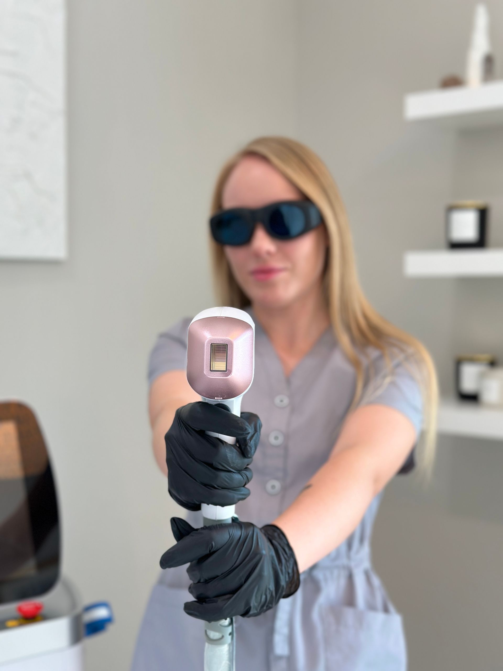 Woman in scrubs and safety glasses holds a laser hair removal device.