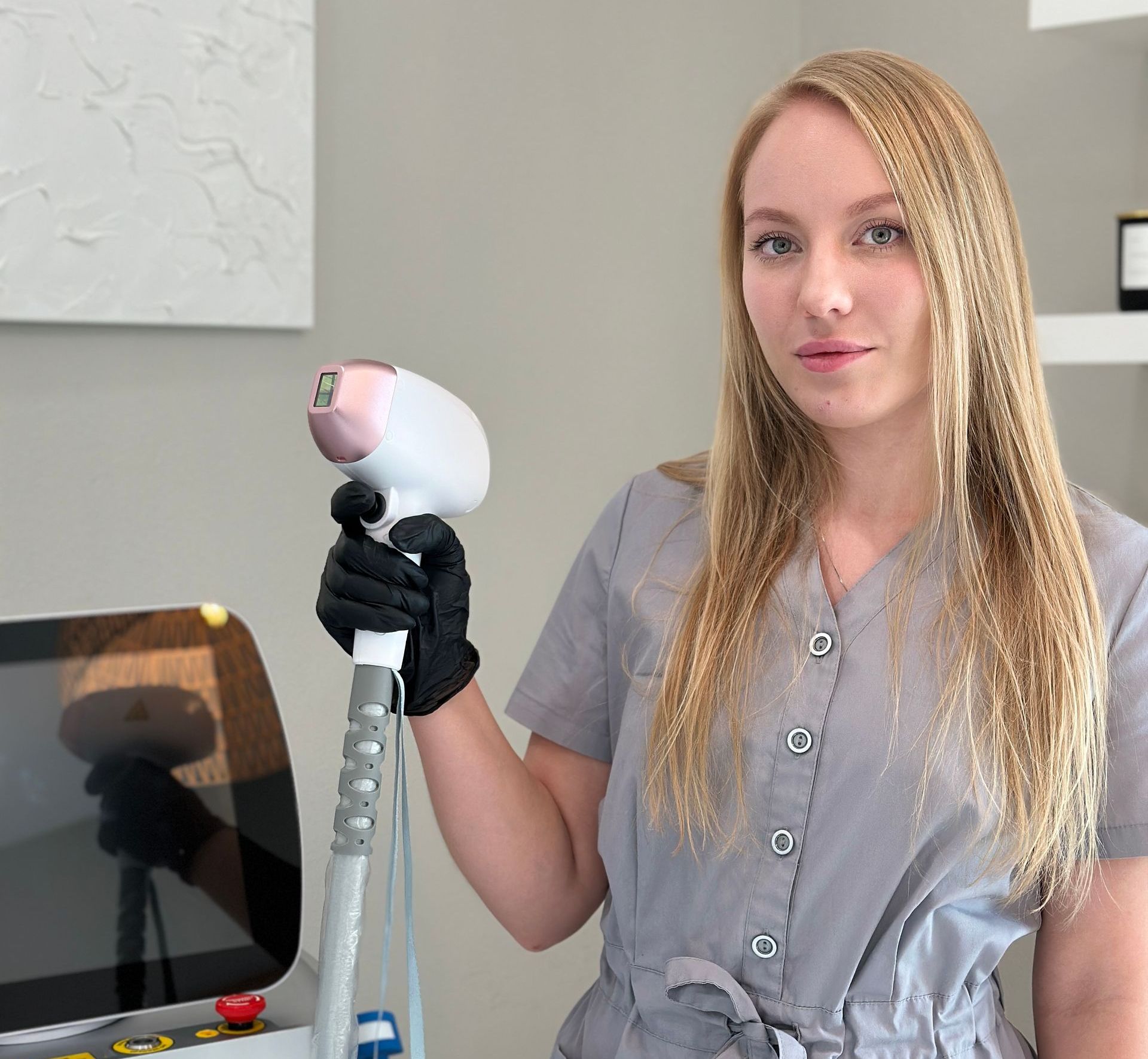 Woman in gray uniform holds a laser hair removal device.