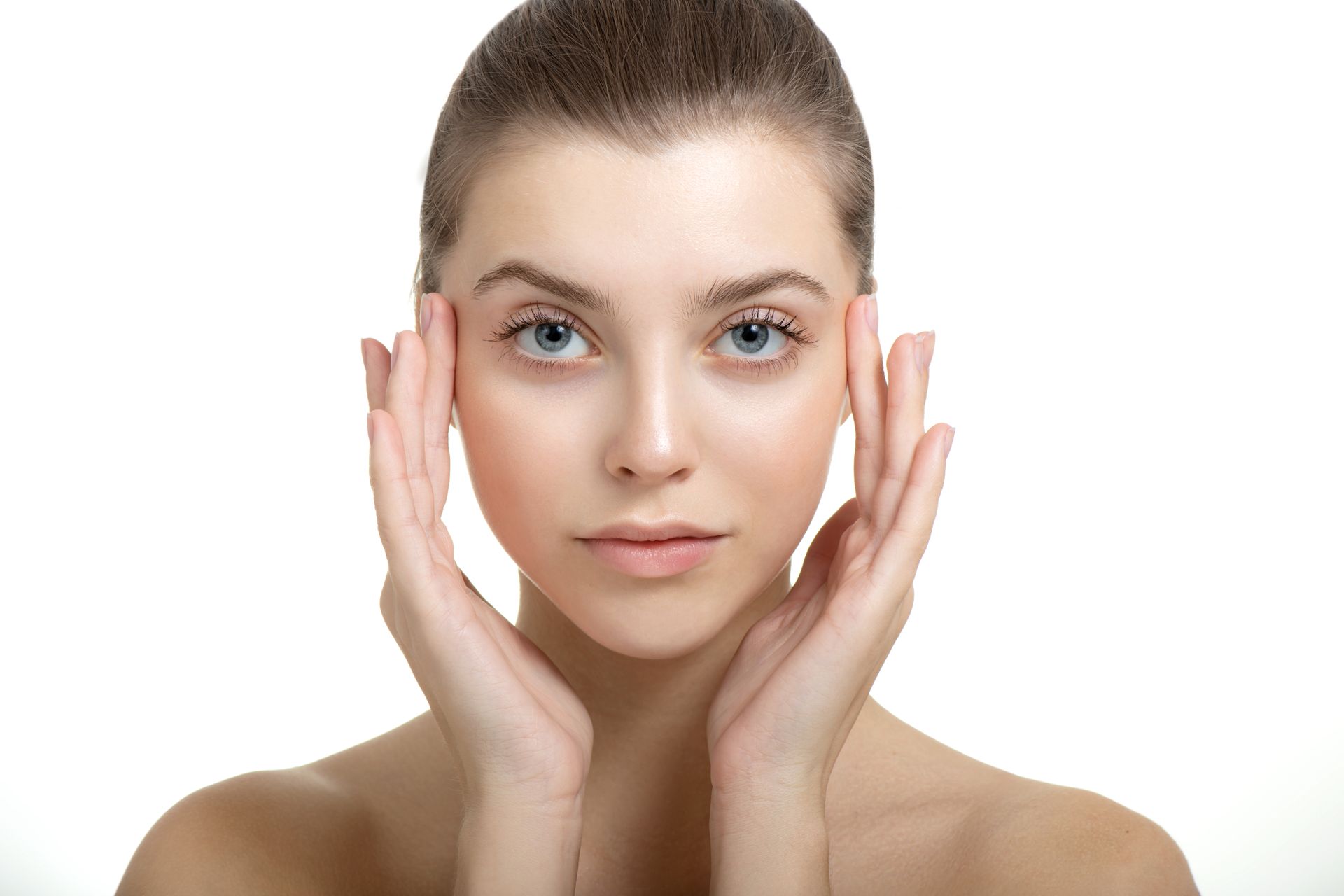 Woman with hands framing her face, looking at the camera. Skin is fair, background white.