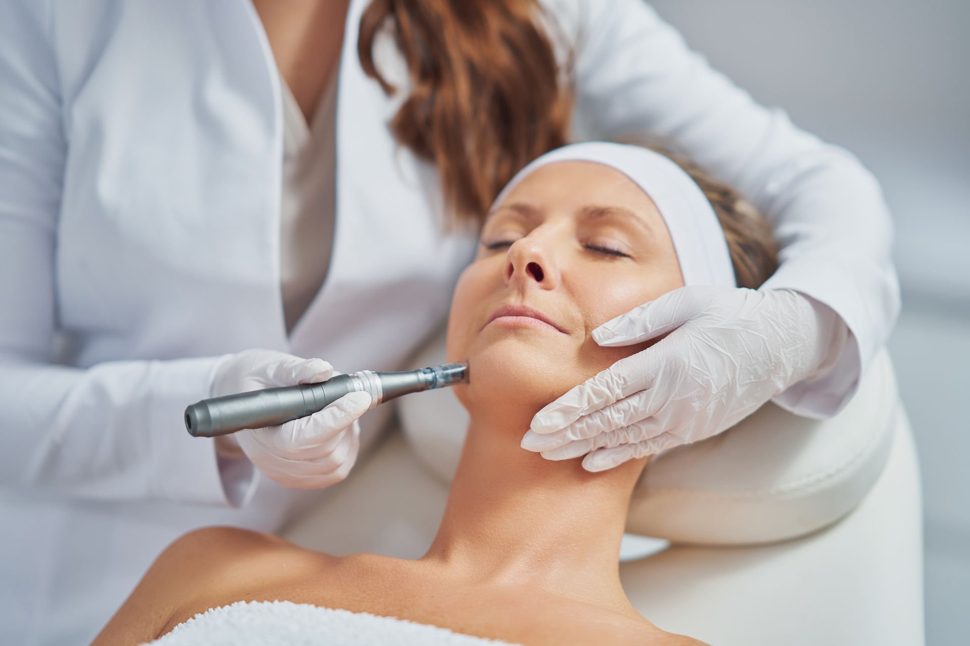 Person receiving a cosmetic treatment to the face and neck. A person in white coat and gloves is operating a skin treatment tool.