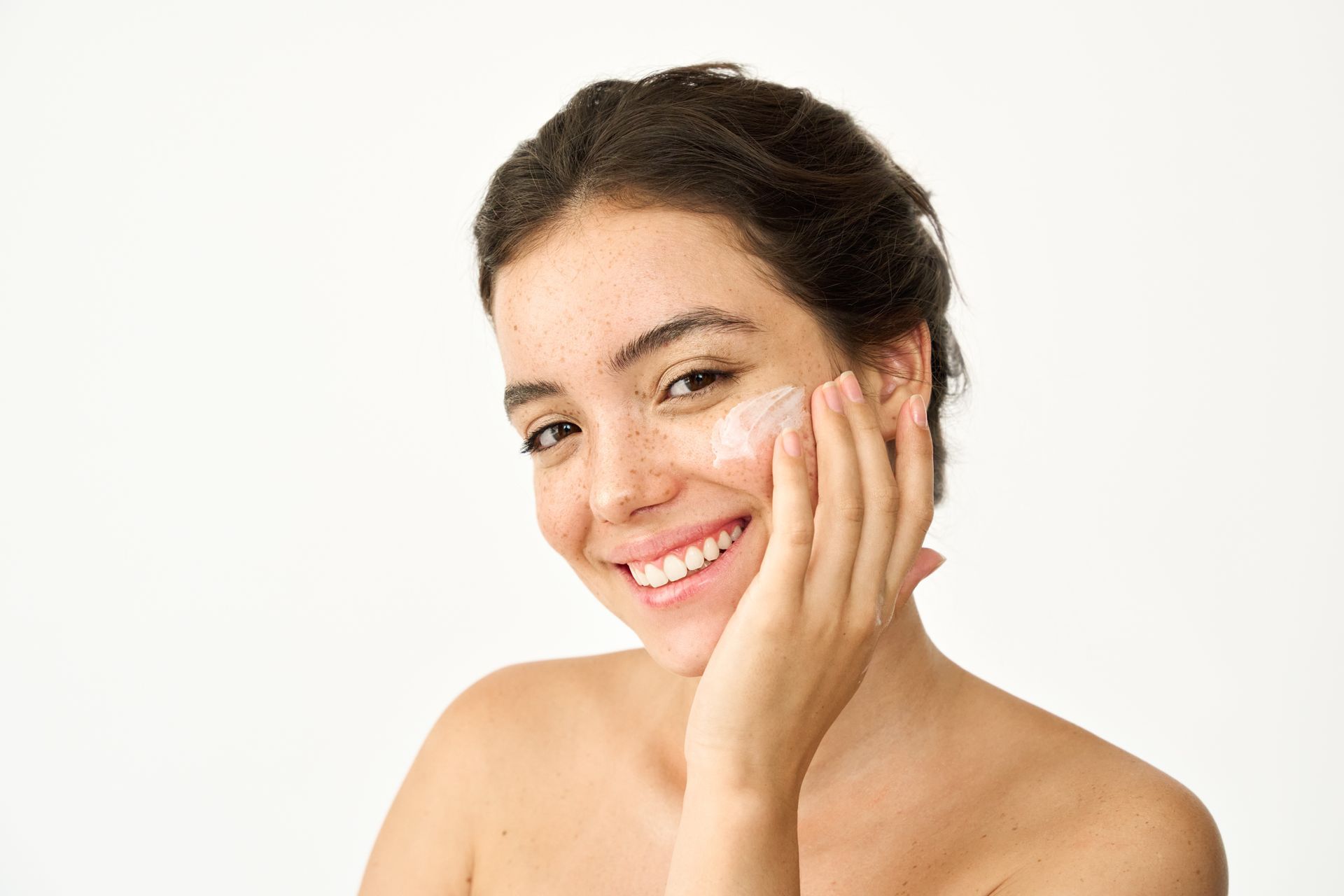 Woman applying skincare product to her face, smiling. White background.