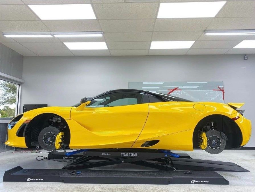 Man polishing a black car in a well-lit garage using a power tool.