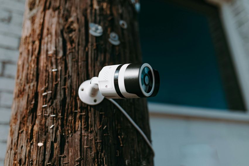 White security camera mounted on a wooden pole, aimed outward near a building window