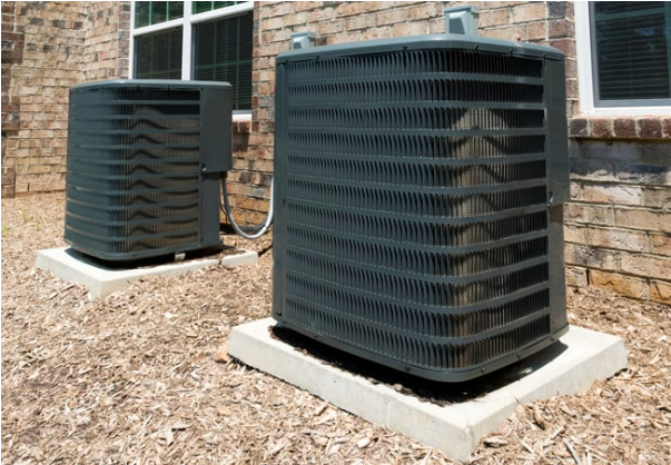 Two air conditioners are sitting outside of a brick building.