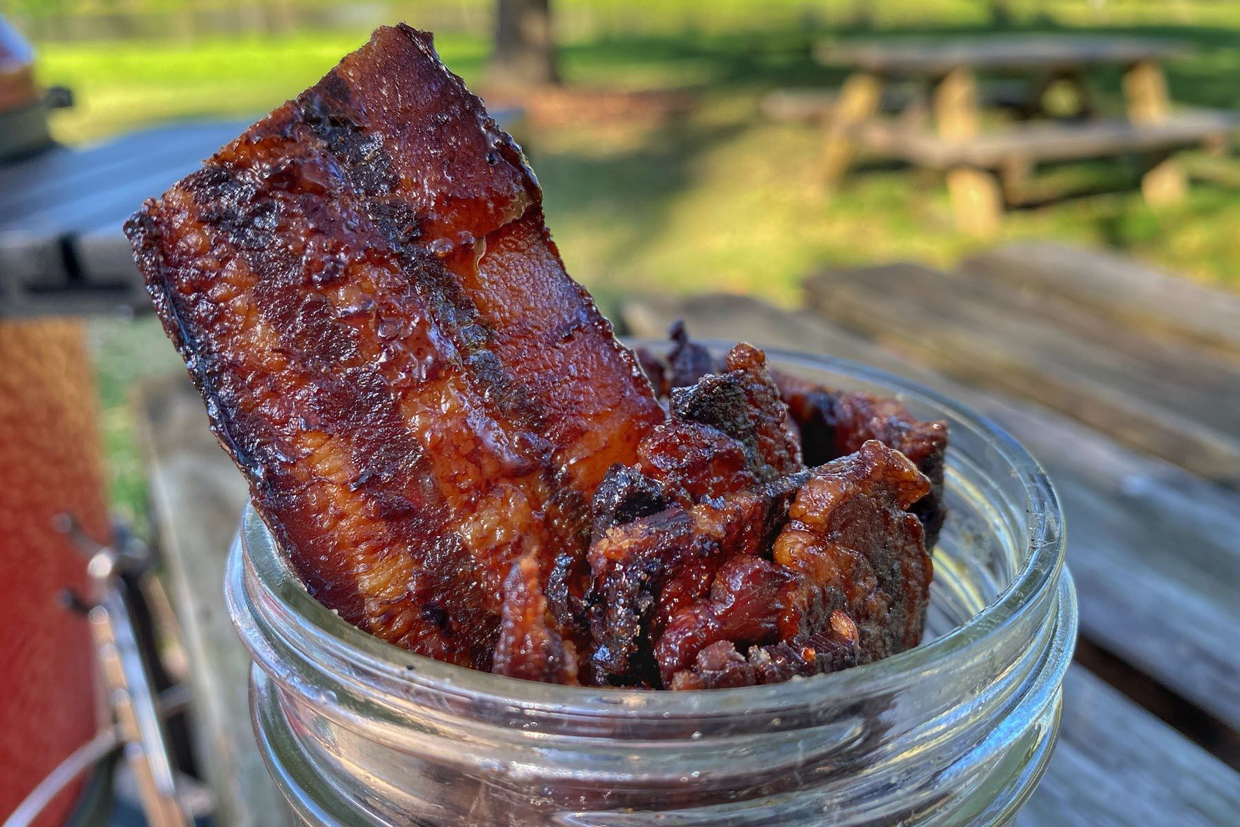 A jar filled with smoked bacon candy is sitting on a wooden table.