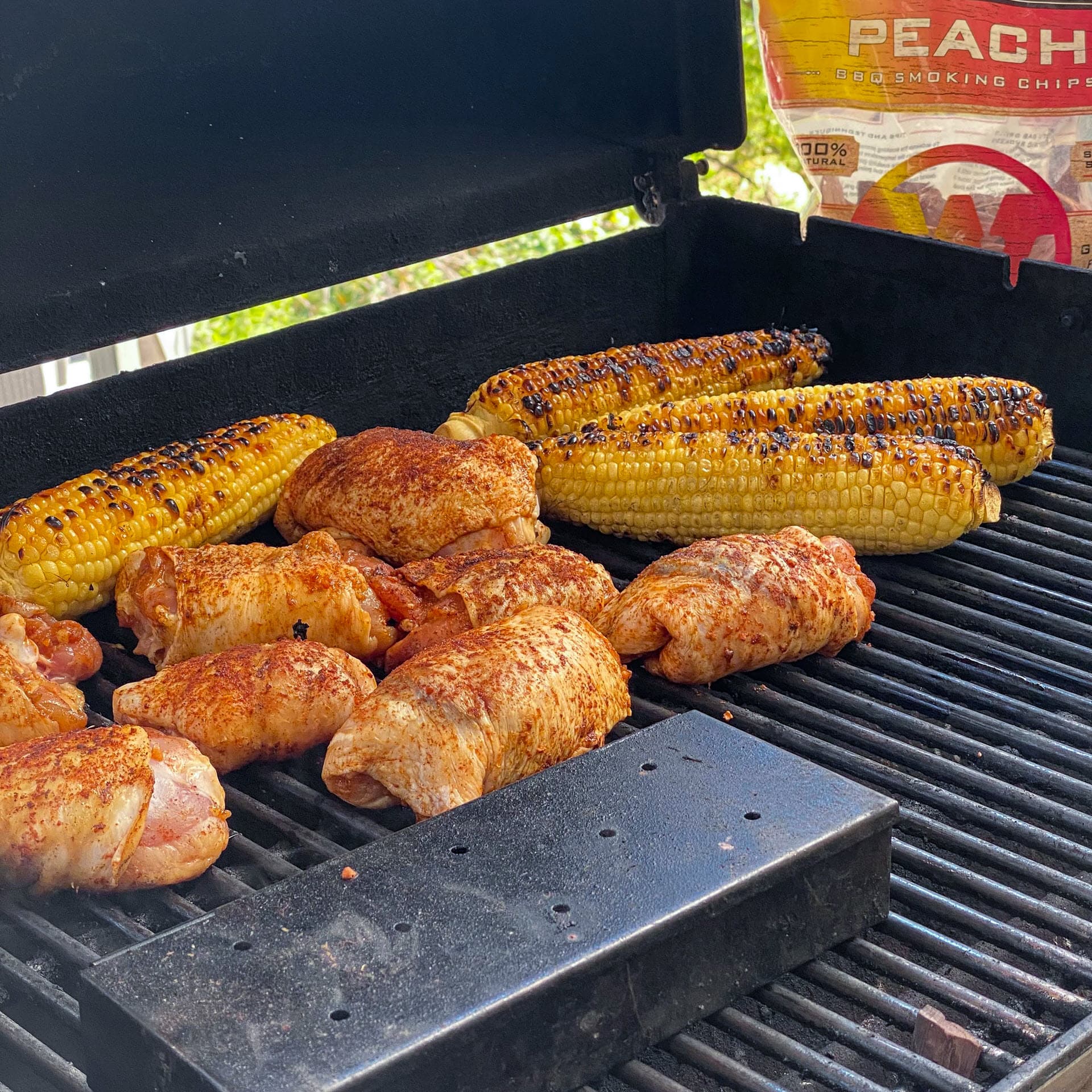 seasoned chicken thighs and corn cooking on grill with peach smoking chips