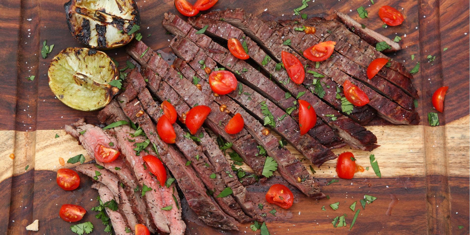 Grilled flank steak slices with cherry tomatoes and roasted vegetables on a wooden board