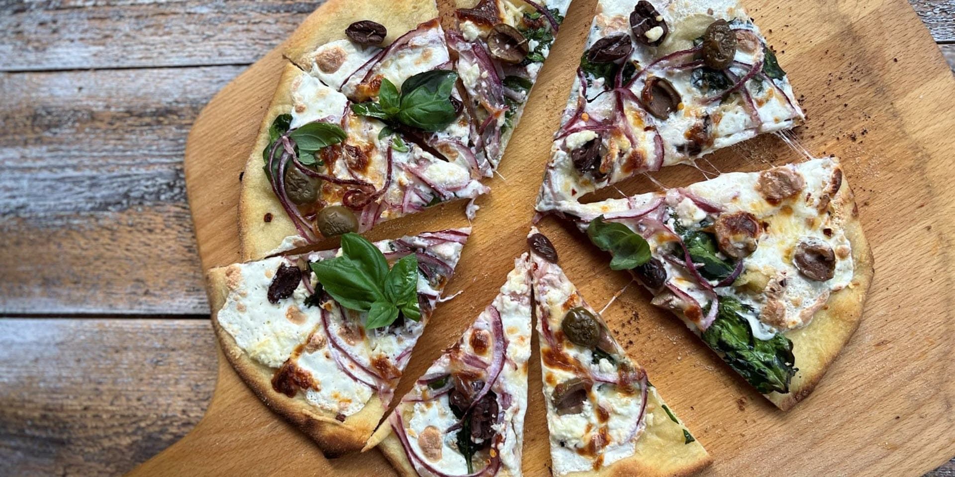 A sliced pizza with vegetable toppings is sitting on a wooden cutting board.