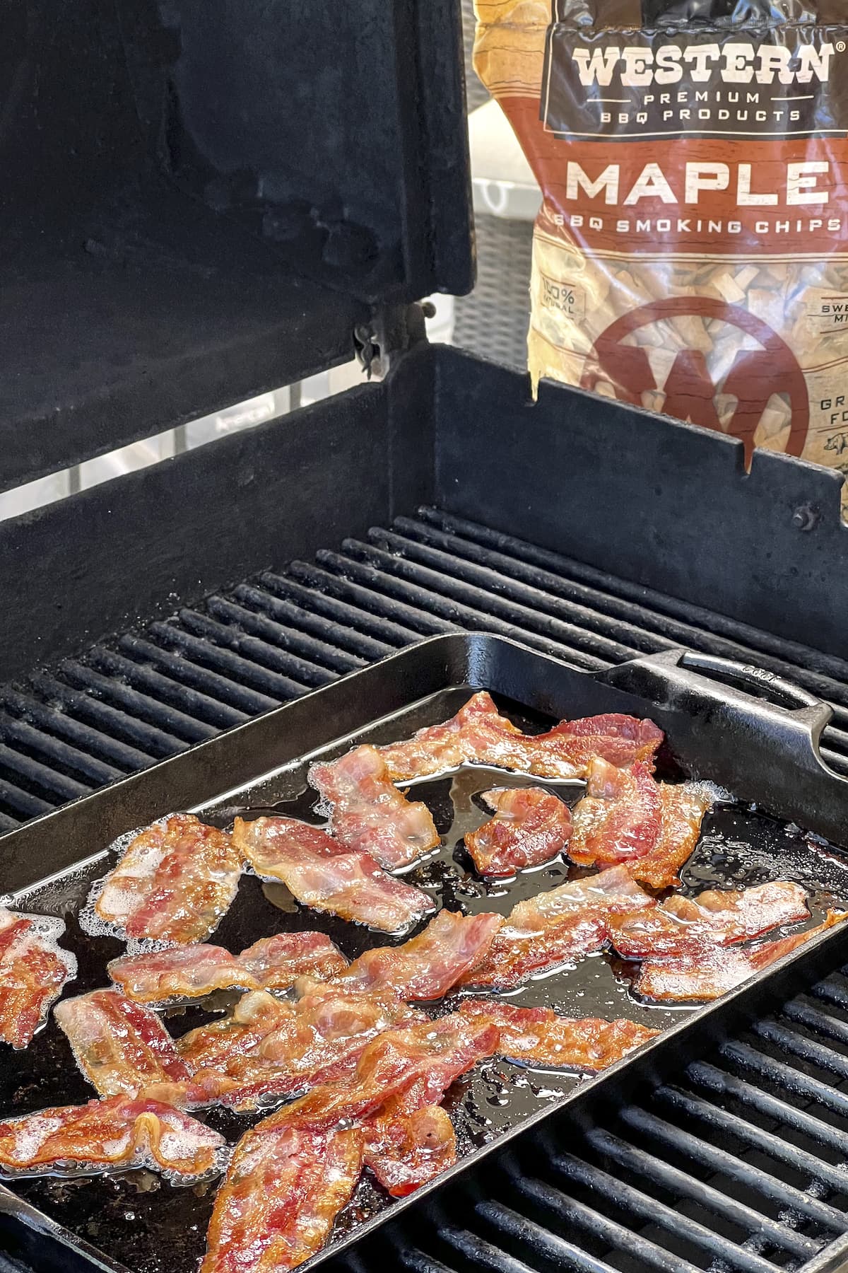 bacon cooking on the grill with bag of maple bbq smoking chips