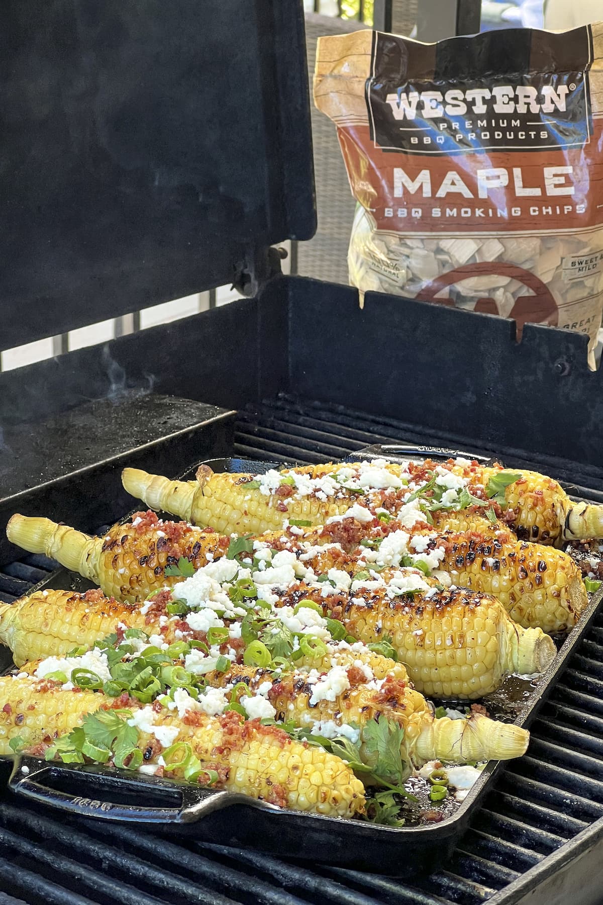 corn on the cob covered in onions, bacon and queso fresco, with bag of maple bbq smoking chips