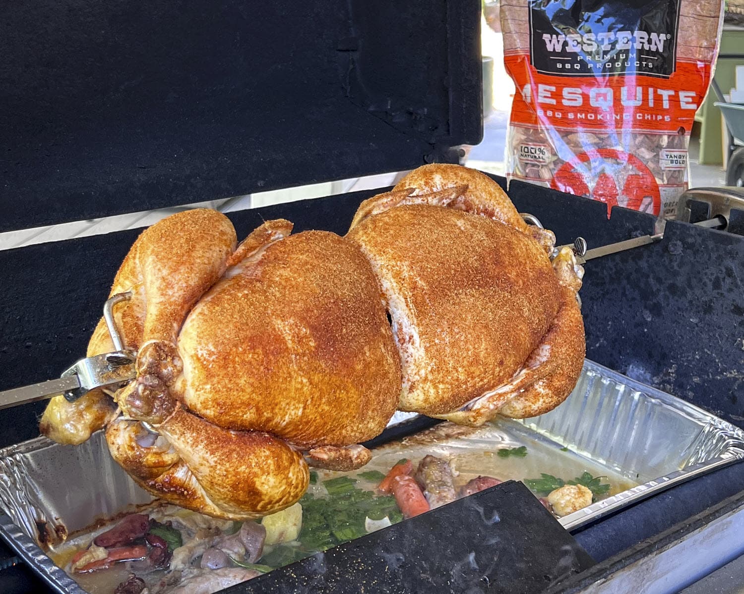 Spiced Rotisserie chickens on spit rod with Western Mesquite Smoking Chips bag in background