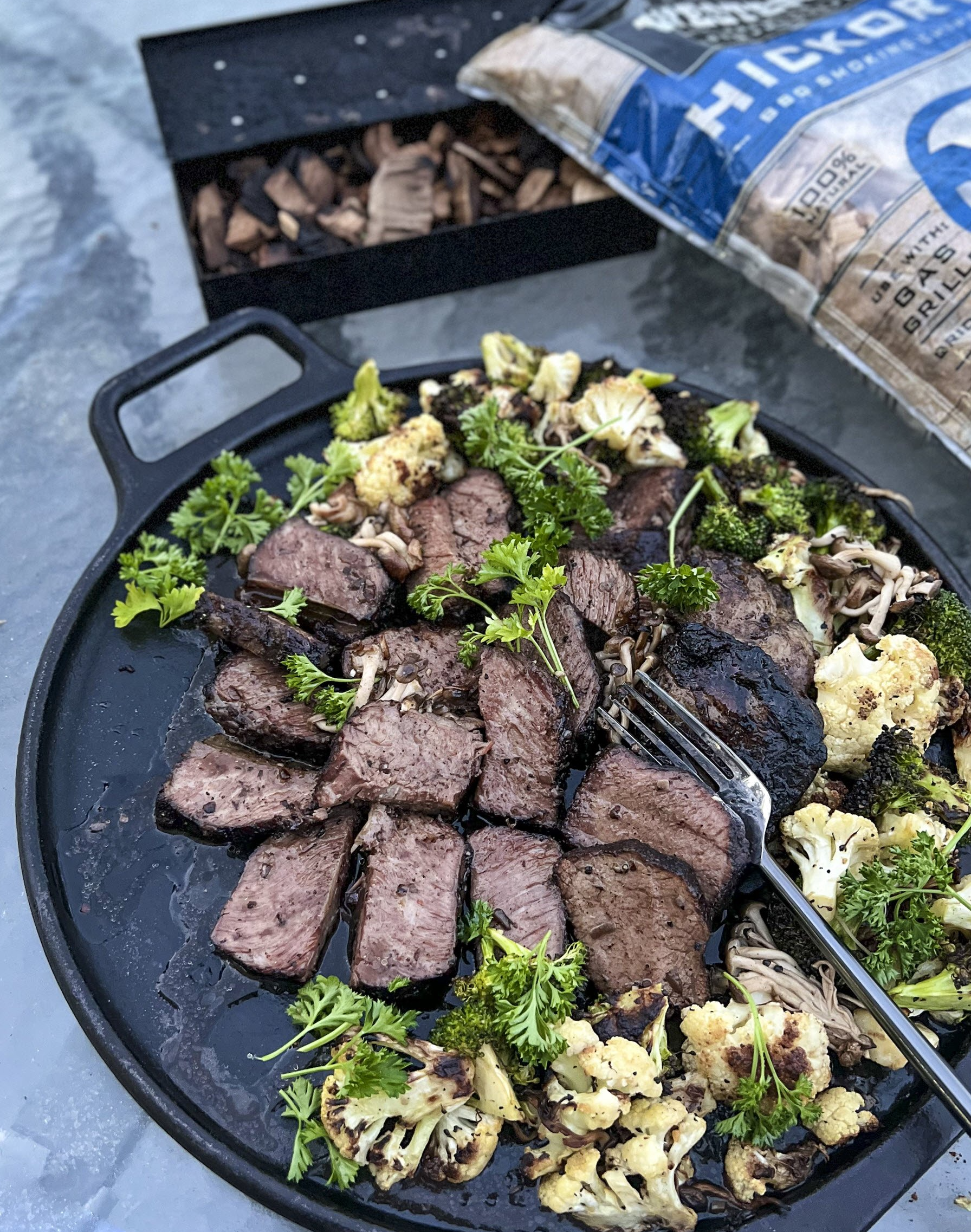 A cast iron pizza pan is the serving platter for cauliflower, broccoli, and smoked short ribs.