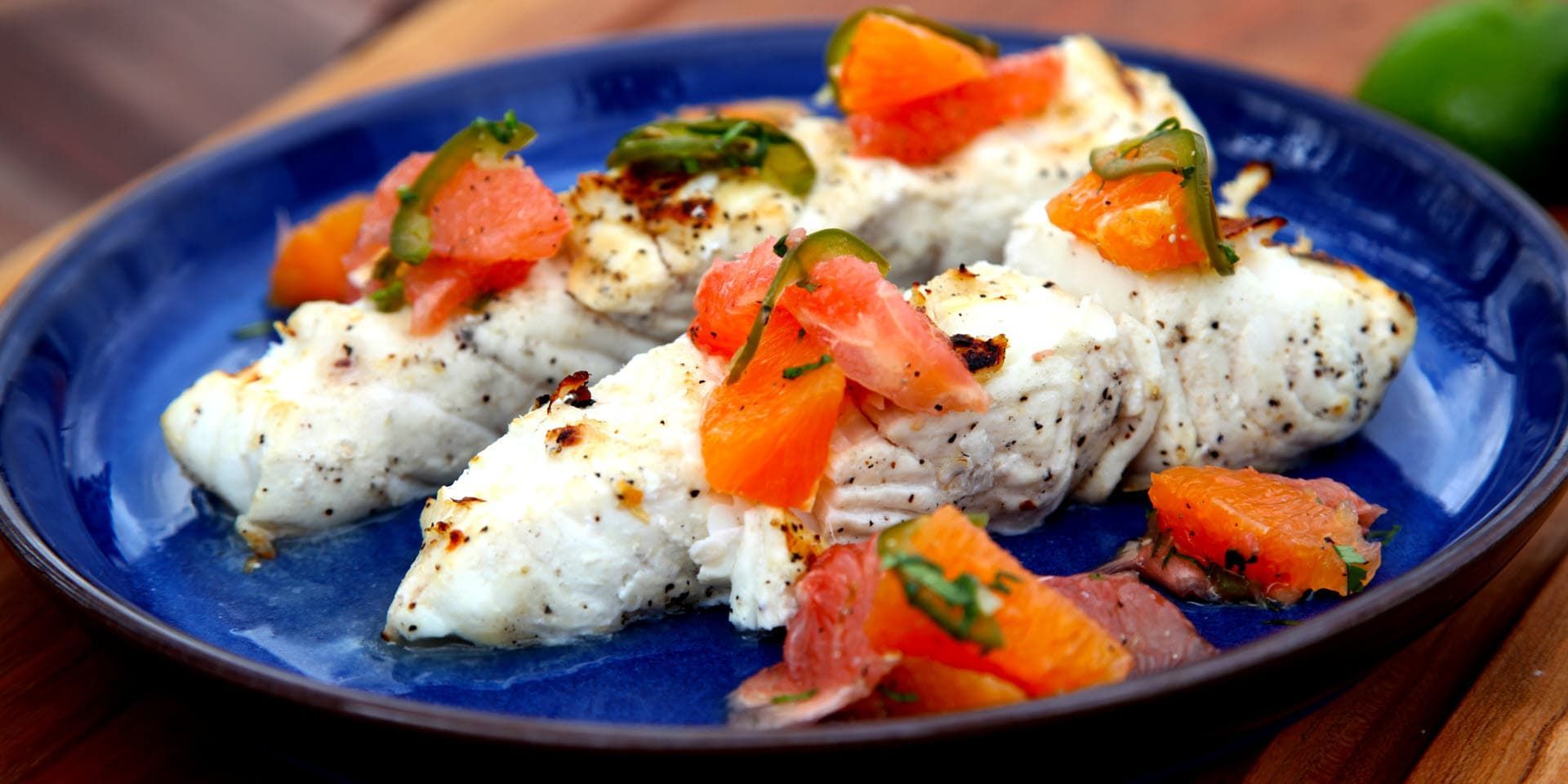 A blue plate topped with mahi mahji and vegetables on a wooden table.