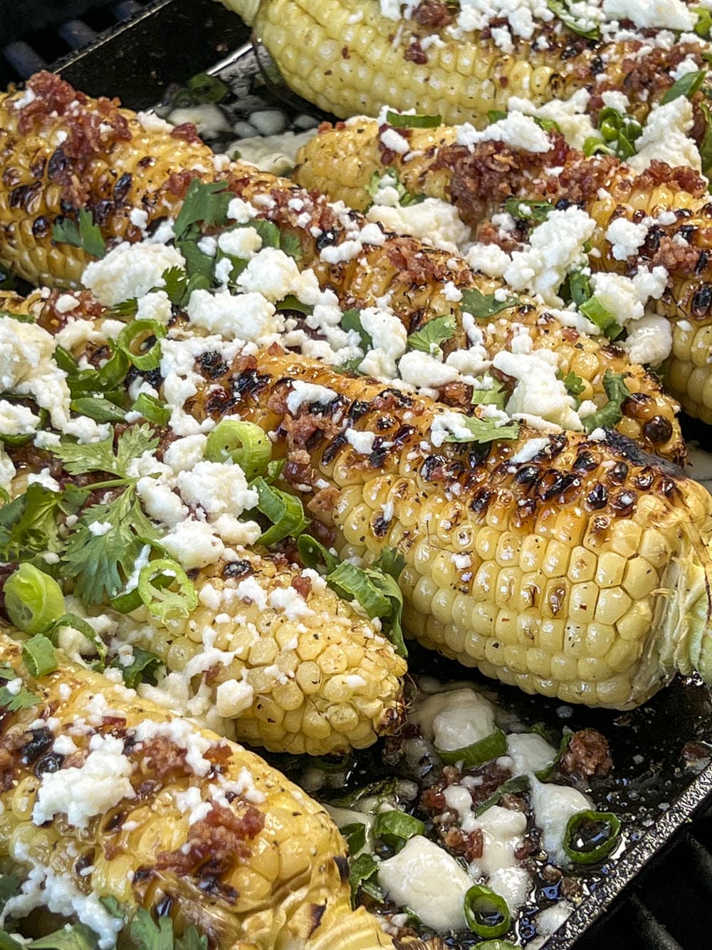 Grilled Corn on the cob topped with onions, cilantro, queso fresco and bacon