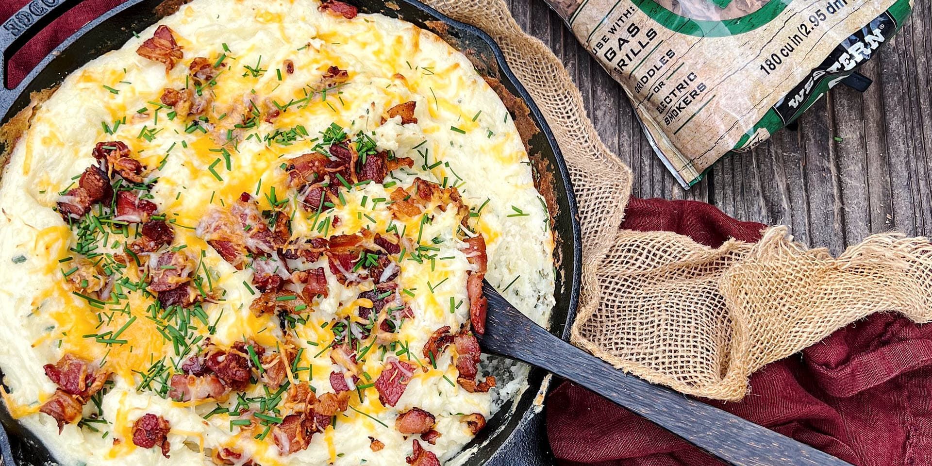 A skillet filled with mashed potatoes and bacon next to a bag of rice.