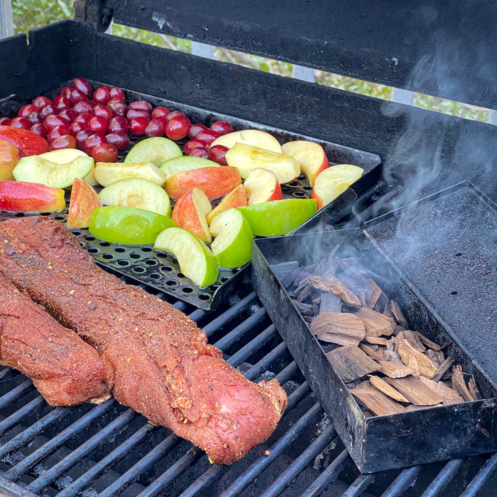 seasoned pork tenderloins and fruit cooking on grill with apple BBQ smoking chips