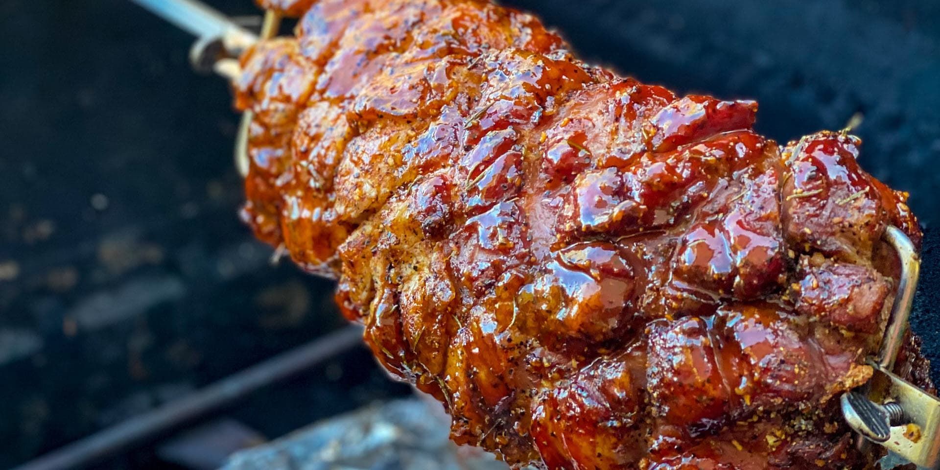 A pork loin is being cooked on a skewer on a grill .