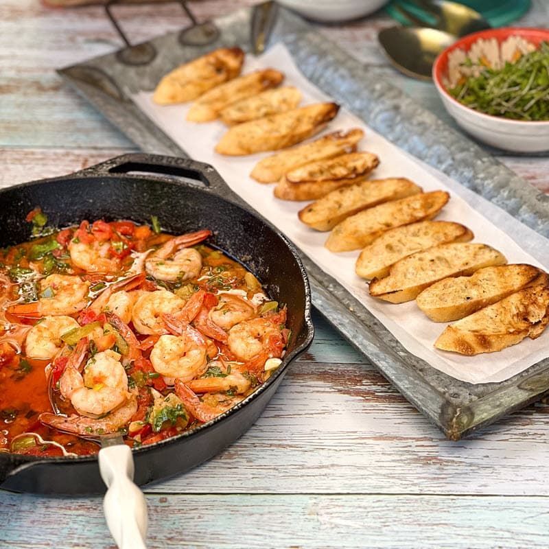 Shrimp scampi in pan with plate of grilled bruschetta baguettes
