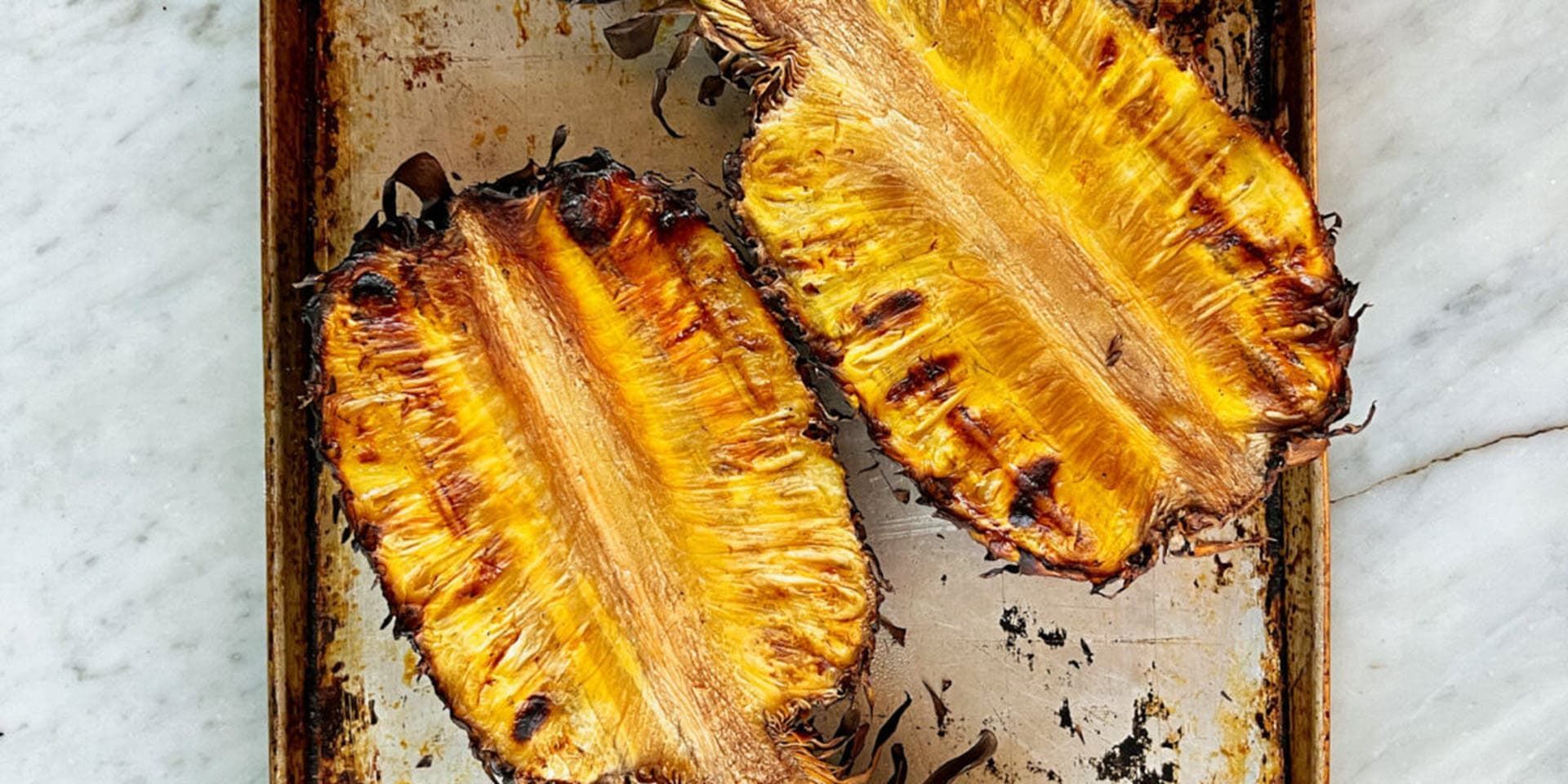 Two grilled pineapples are sitting on a pan on a table.