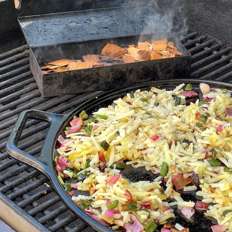 Hash browns with peppers and onions in cast iron pan with wood chips smoking in a smokebox on the grill