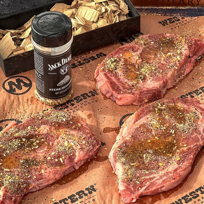 Smoking wood chips in smokebox, Jack Daniel's® Steak Seasoning, and 3 oiled and seasoned raw steaks