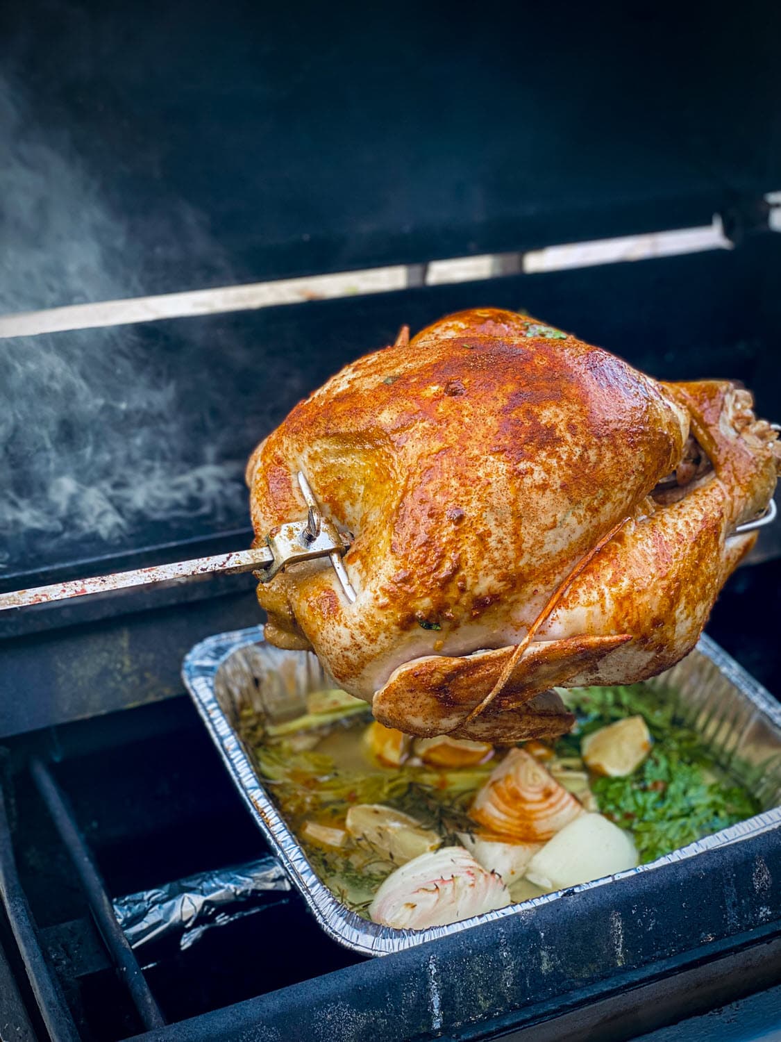 whole turkey cooking on rotisserie grill with smoke from apple smoking chips