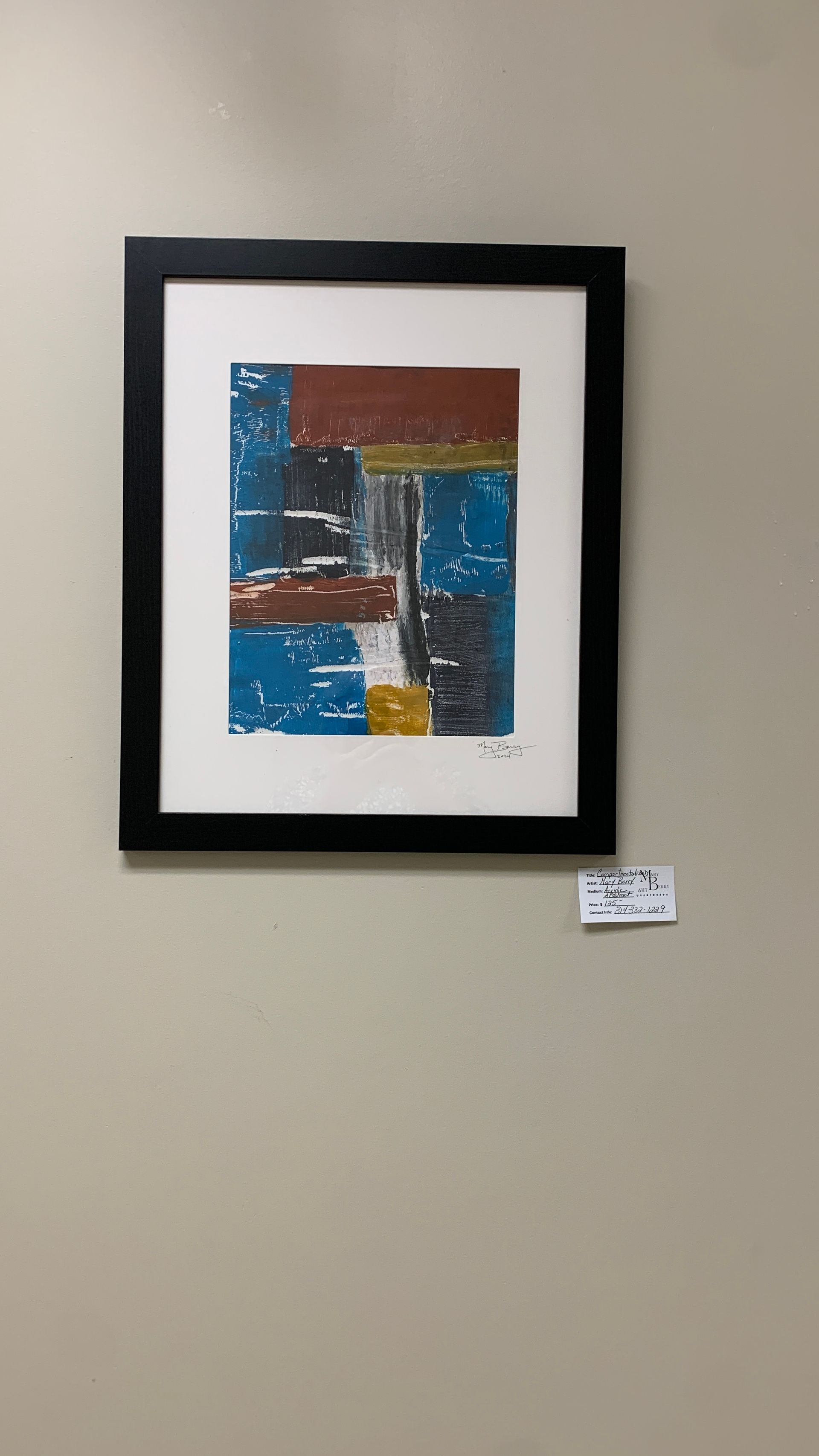 Abstract painting in a black frame on a tan wall. Blue, red, and yellow blocks of color.  By Mary Berry - Art