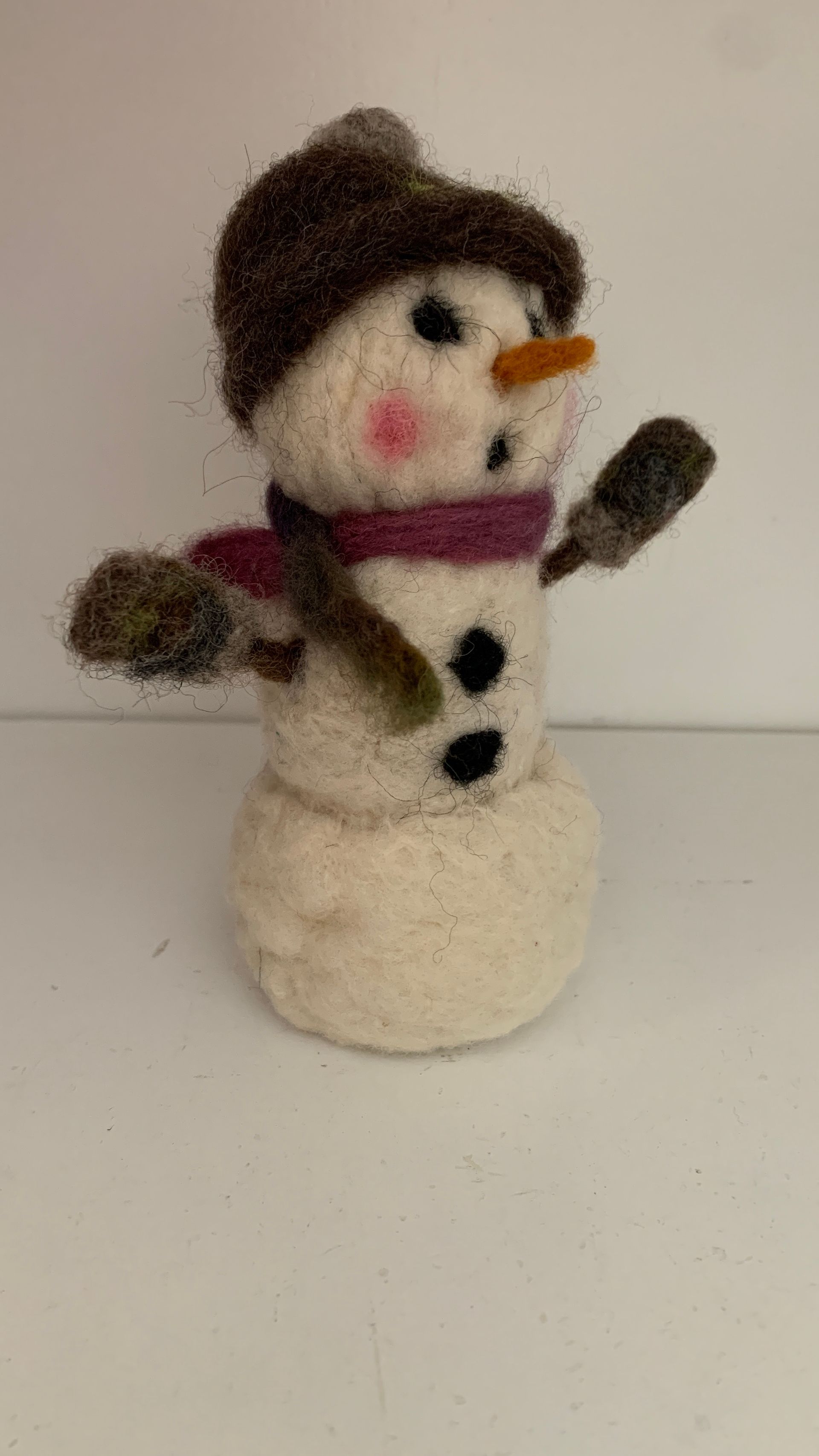 Snowman made of felt wearing hat, scarf, and mittens; on a white surface.  By Mary Berry - Art