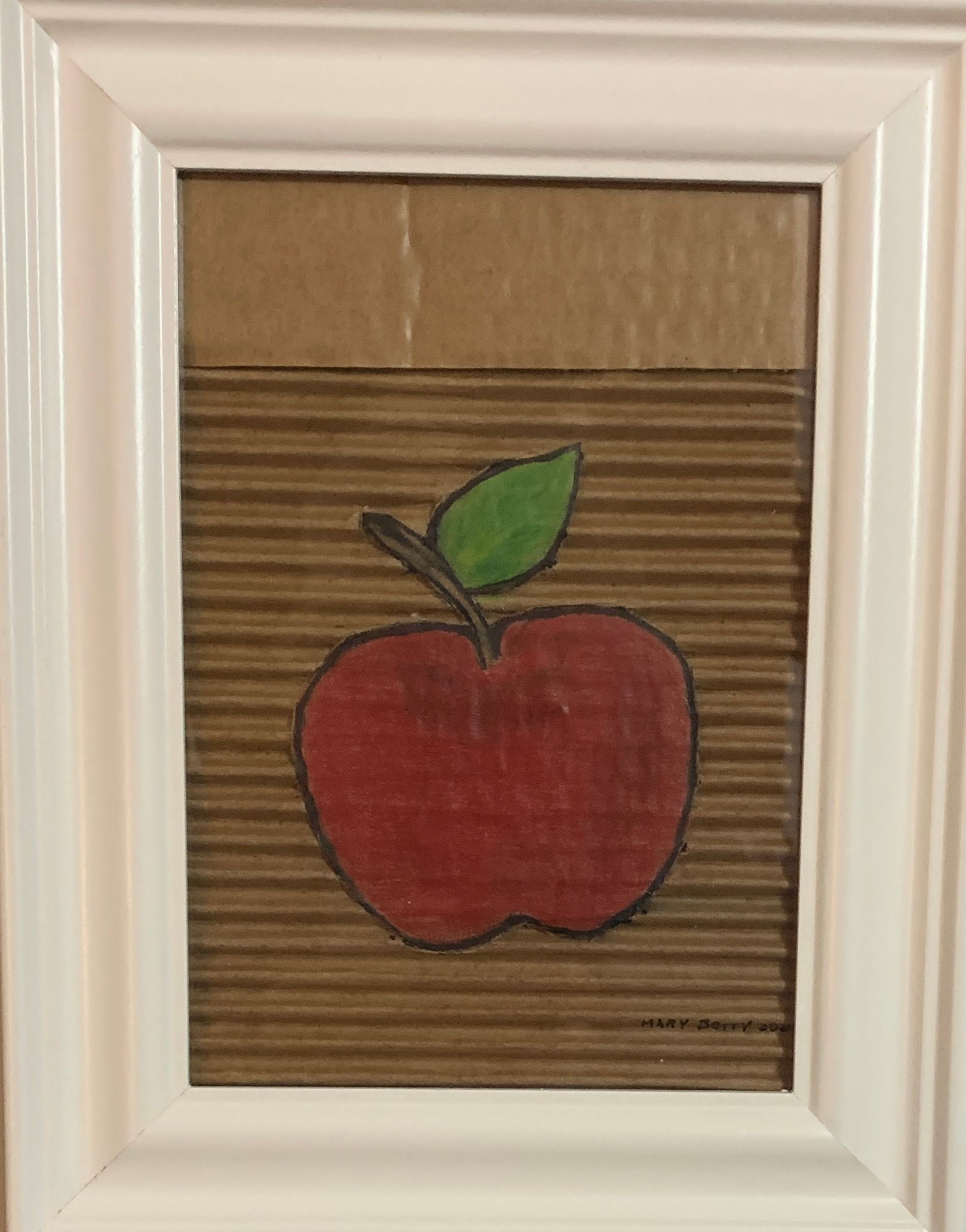 Red apple drawing with green leaf on corrugated cardboard background, framed in white.  By Mary Berry - Art
