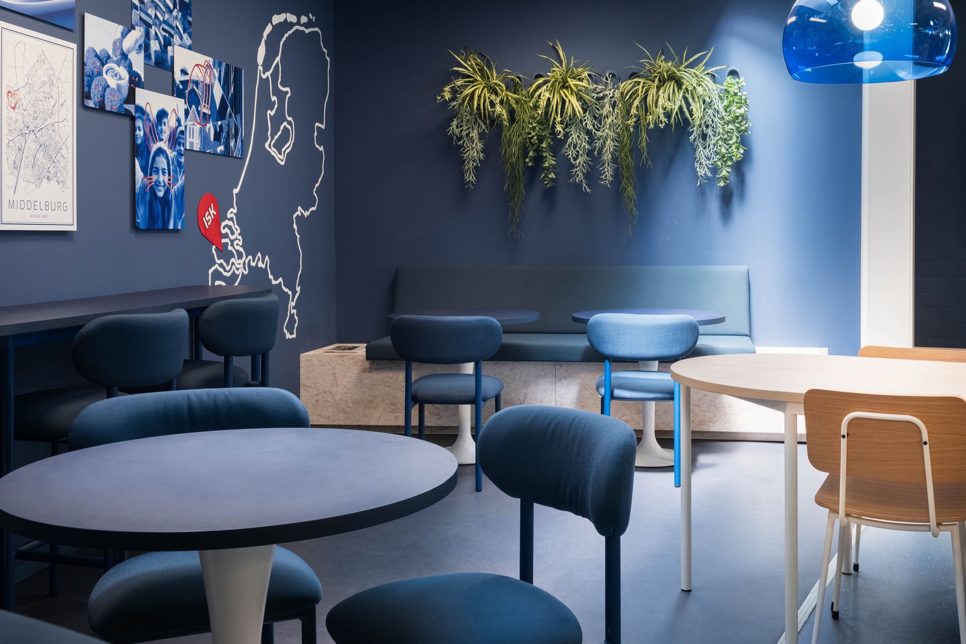 Een moderne kamer in blauwe tinten met ronde tafels, stoelen, een bank, wanddecoratie en hangplanten.