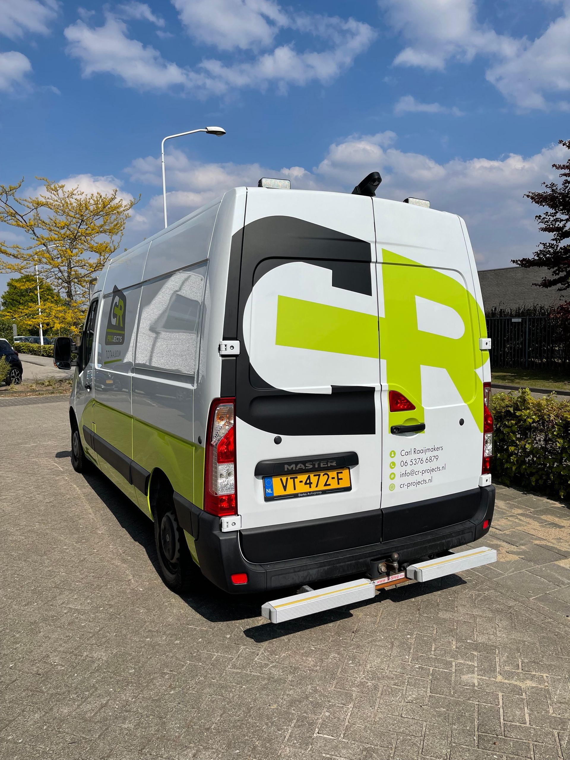 Een wit busje met een groot cr-logo op de achterkant staat geparkeerd aan de kant van de weg.