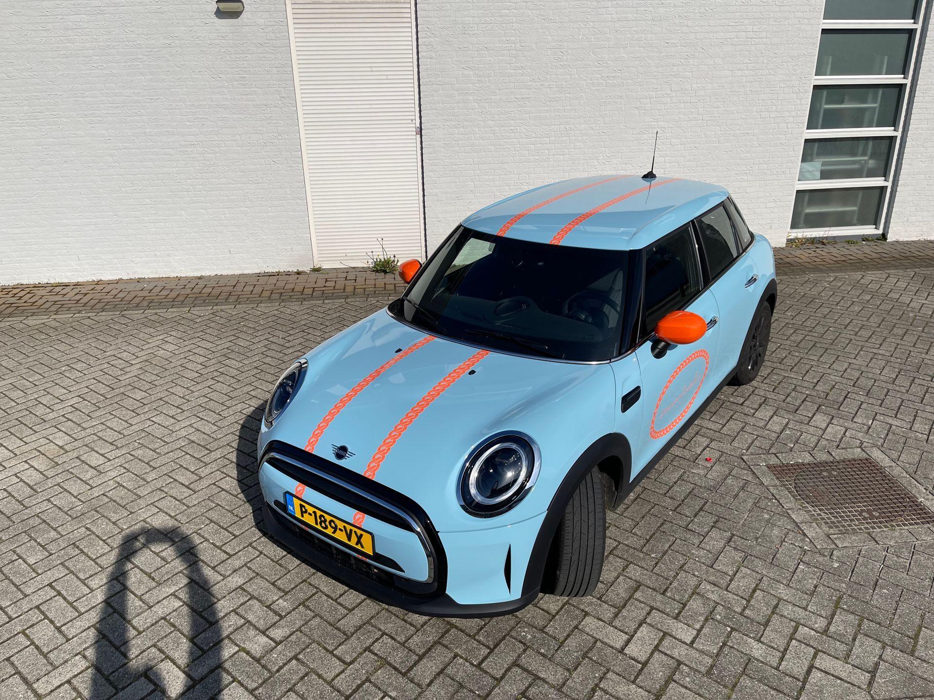 Een blauwe Mini Cooper met oranje strepen staat geparkeerd op een parkeerplaats.