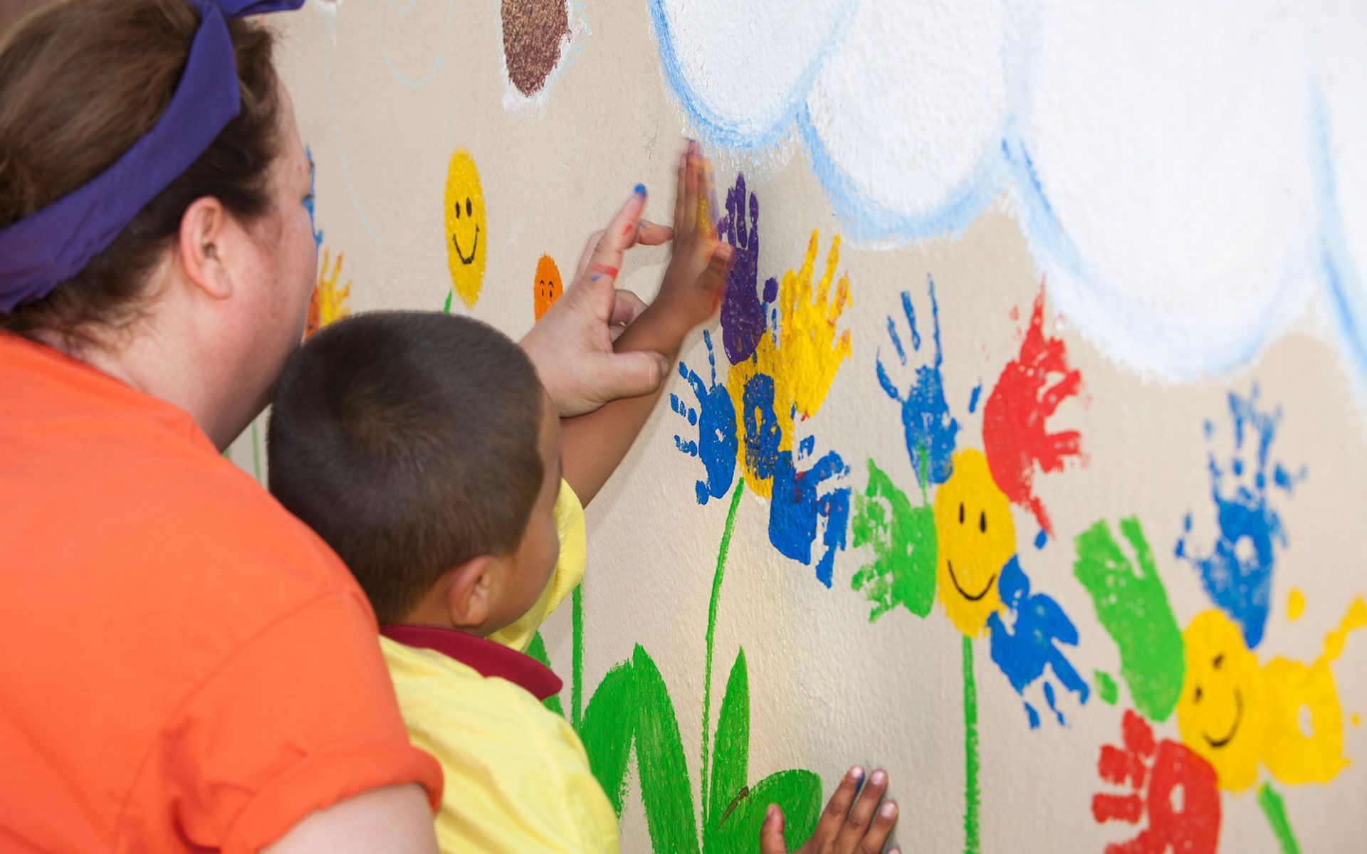 A woman and child are painting flowers on a wall