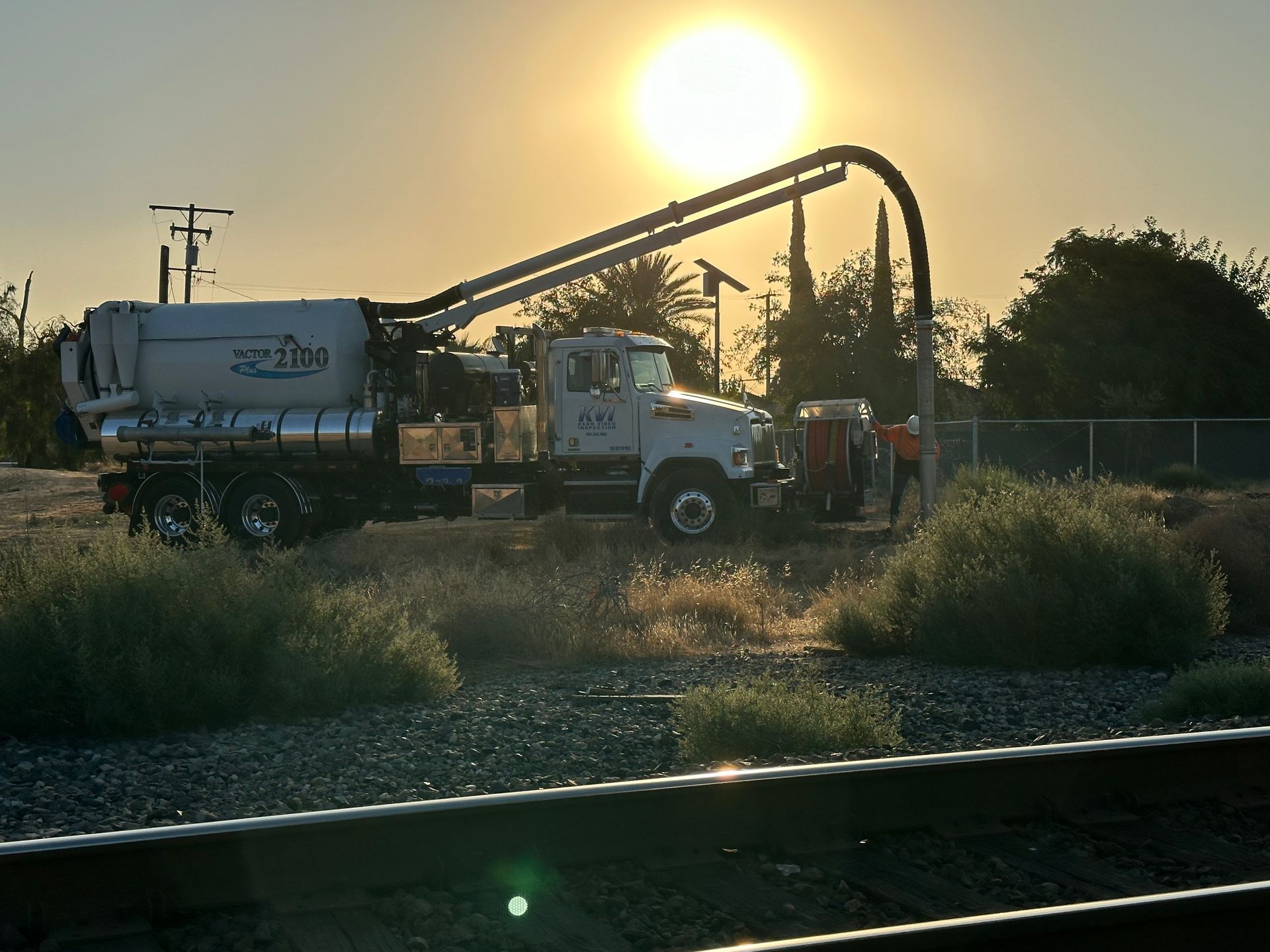 A hydro vac truck is parked next to a train track at sunset.