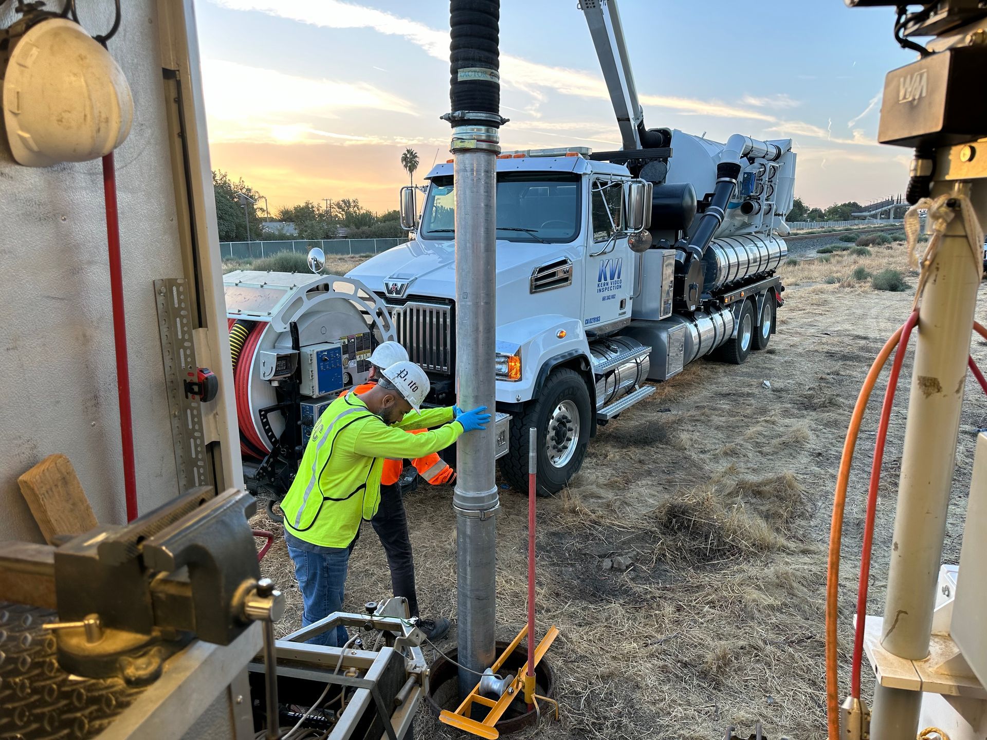 Two men in construction gear and hard hats working on a pipe next to a KVI truck.