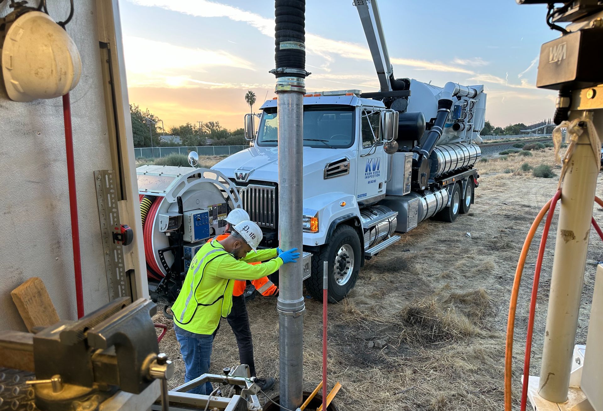 Two men in construction gear and hard hats working on a pipe next to a KVI truck.