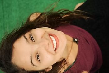 Woman smiling, looking up at camera. She wears a maroon shirt, dark hair, against a green background.