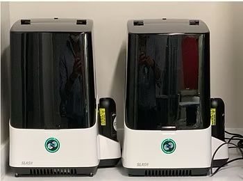 Two white and black humidifiers side-by-side with a person's reflection in the black exterior.