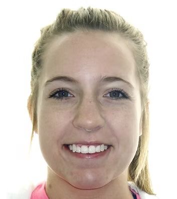 Woman with blonde hair smiling at the camera. She wears a pink top. Bright lighting.