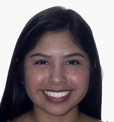 Woman with dark hair, smiling broadly, against a white background.