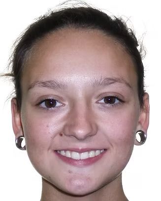 Woman with dark hair pulled back, smiling, wearing large ear gauges.