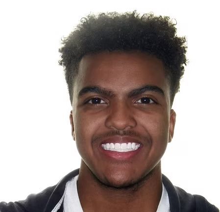 Smiling person with short, dark curly hair, wearing a white shirt and a dark jacket.