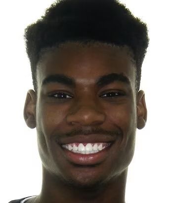 Smiling person with dark skin, short, textured hair, and a visible toothy grin.