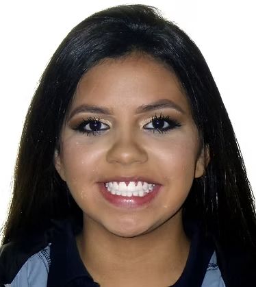 Woman with long dark hair, smiling, wearing makeup, and a blue shirt.