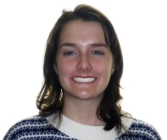 Woman with dark hair smiles, wearing a blue and white patterned sweater.