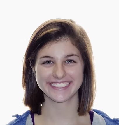 Woman smiling, with short brown hair, wearing a purple shirt under a blue jacket.