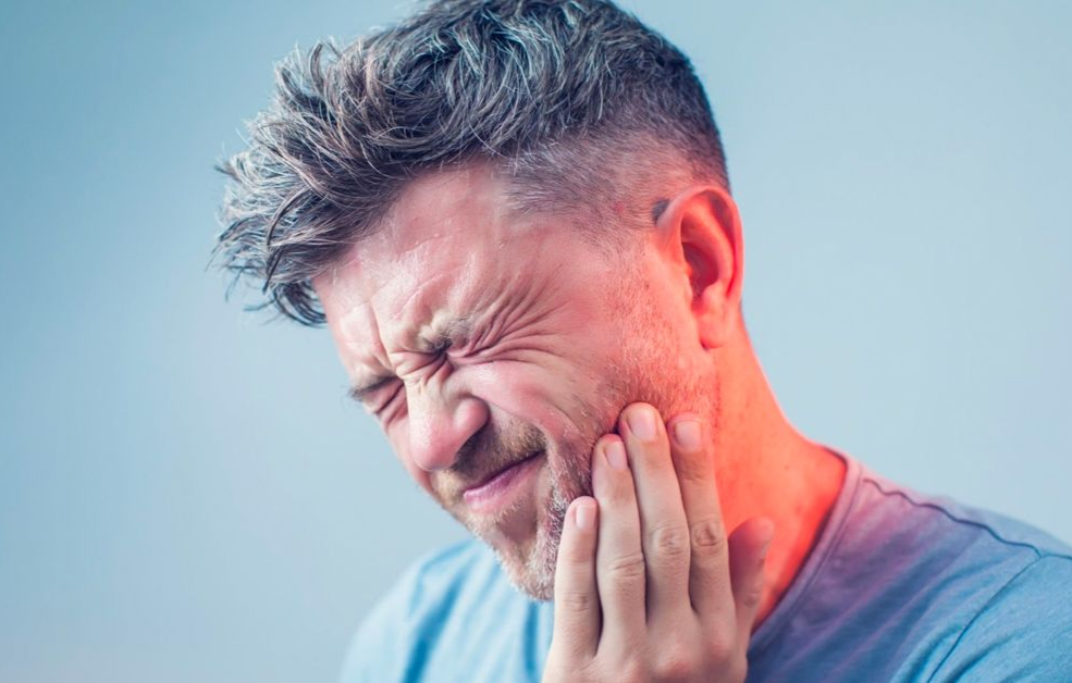 Man in pain, clutching cheek, eyes closed, red glow on face, blue background.