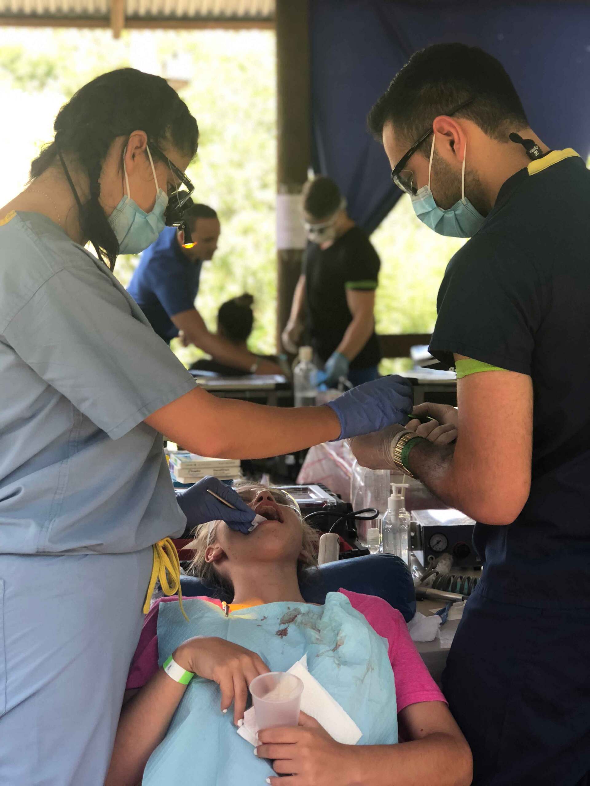 A girl is getting her teeth examined by two dentists